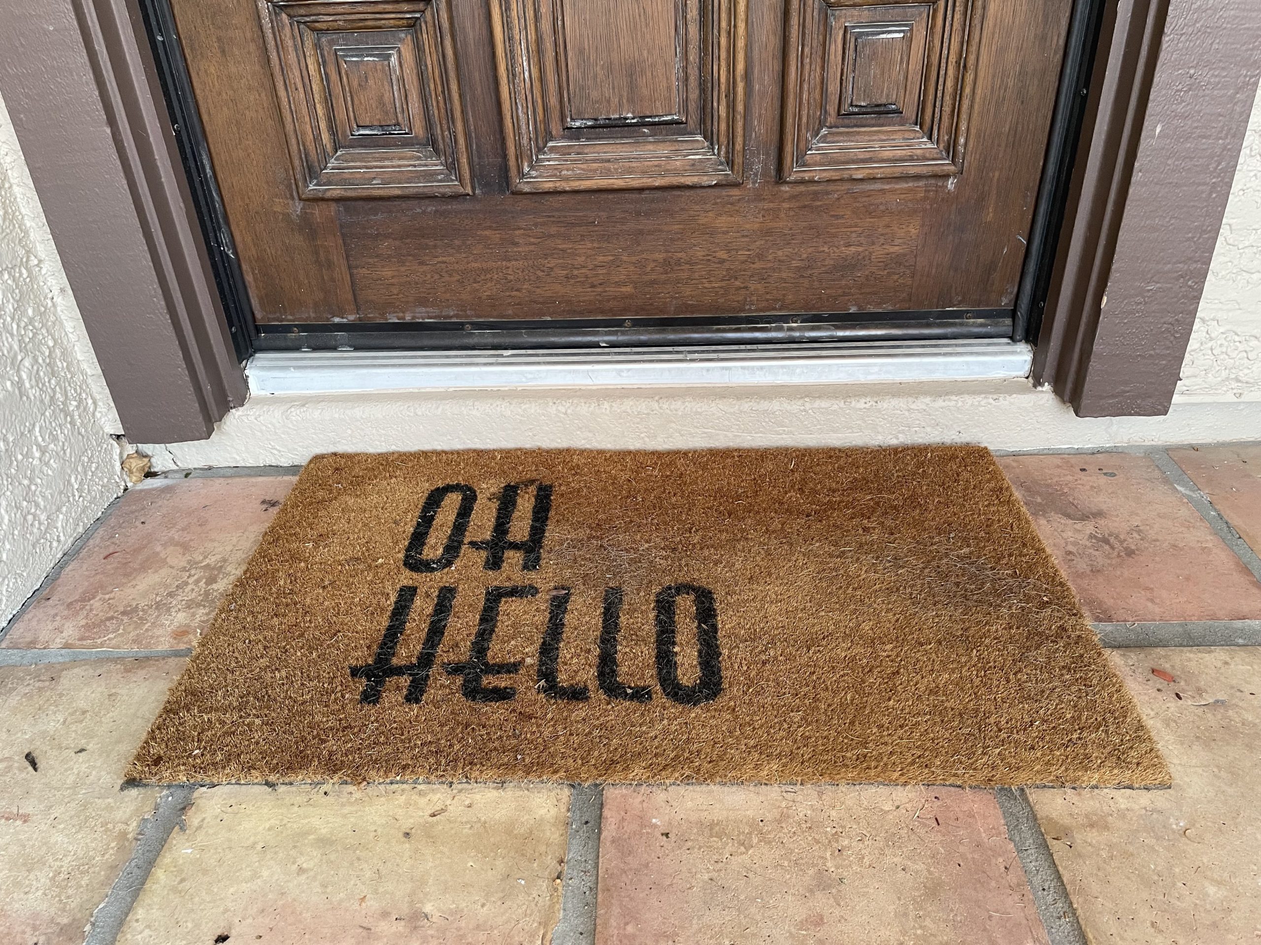 Front door with brown welcome mat that reads "Oh, Hello"